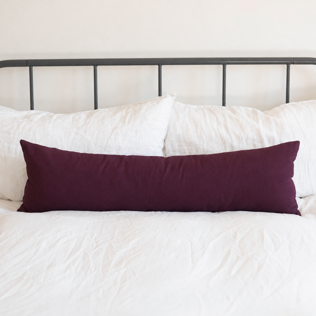 Deep burgundy rectangular body pillow on white bedding with metal headboard.