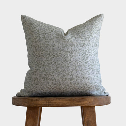 Gray and white floral patterned linen pillow displayed on a wooden stool.