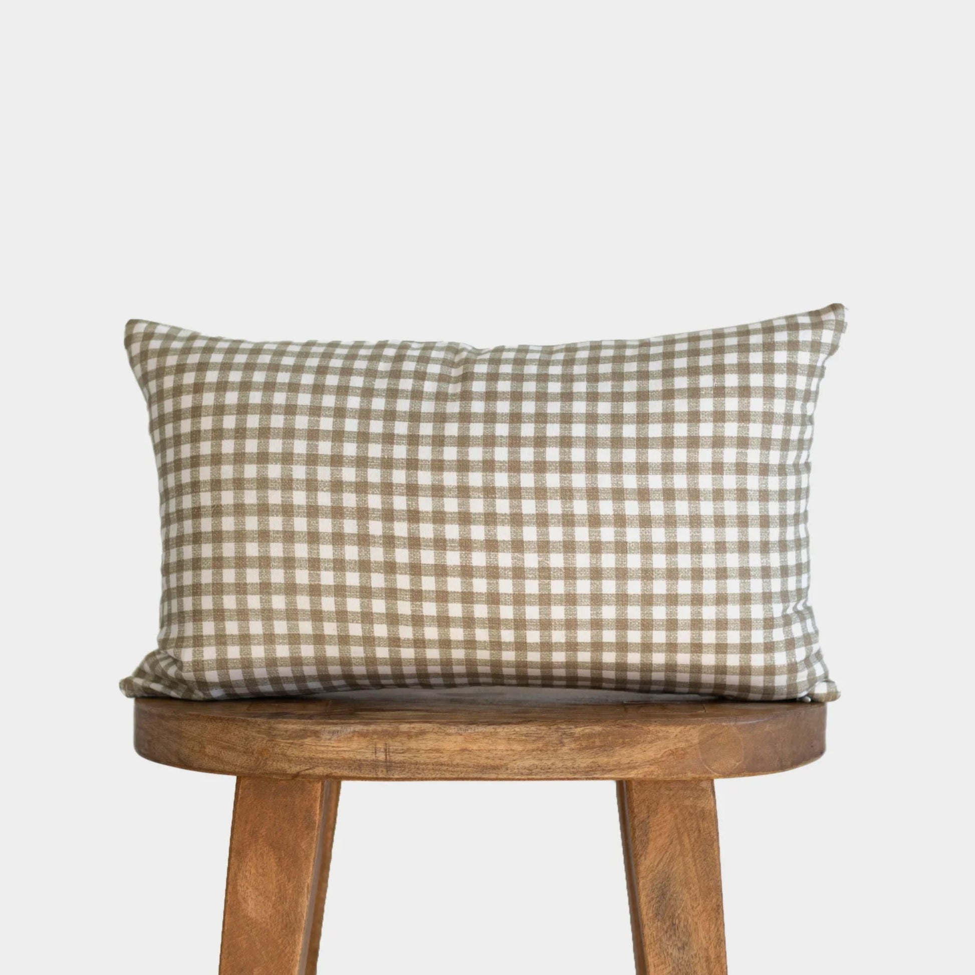 Rectangular lumbar pillow with tan and white gingham check pattern resting on wooden stool.