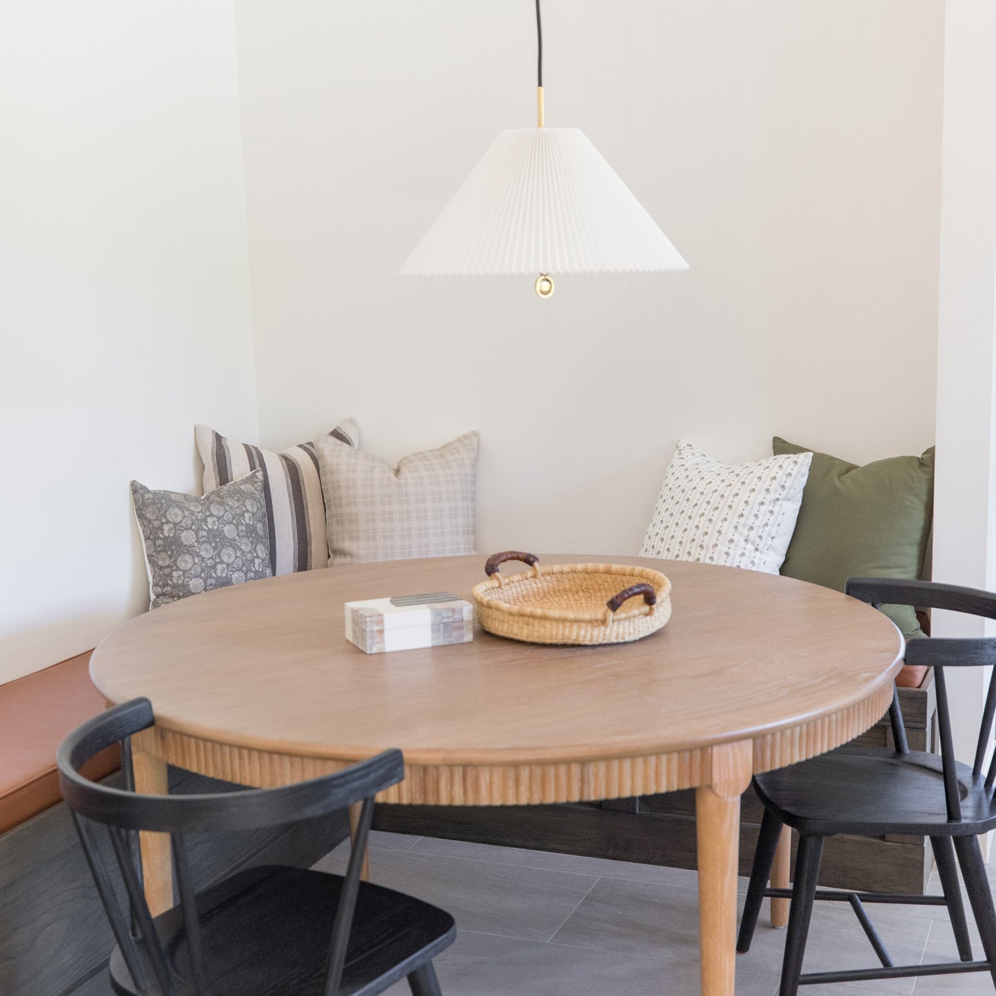 Taupe pleated cone pendant light suspended above a wooden dining table.