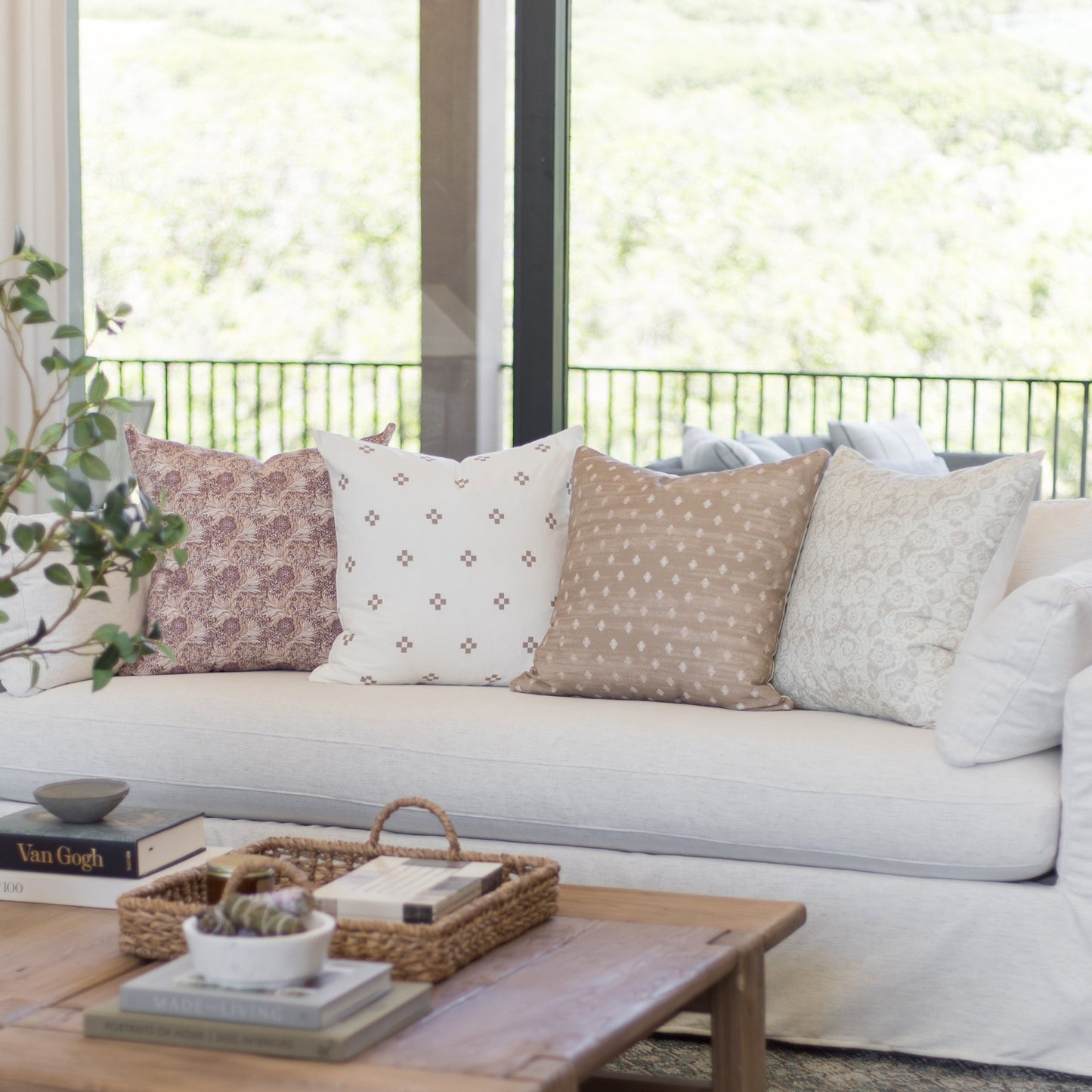 Four patterned throw pillows in pink, cream, tan, and gray displayed on a light gray sofa.