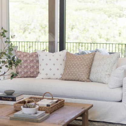 Four patterned throw pillows in pink, cream, tan, and gray displayed on a light gray sofa.