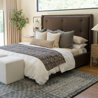 Brown upholstered bed with white bedding, decorative pillows, textured throw blanket, and cream bench at foot.