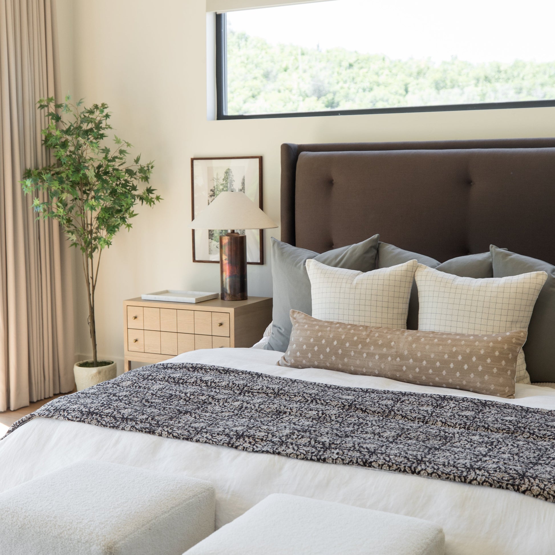 Dark speckled throw blanket draped across a bed with patterned pillows in a modern bedroom setting.