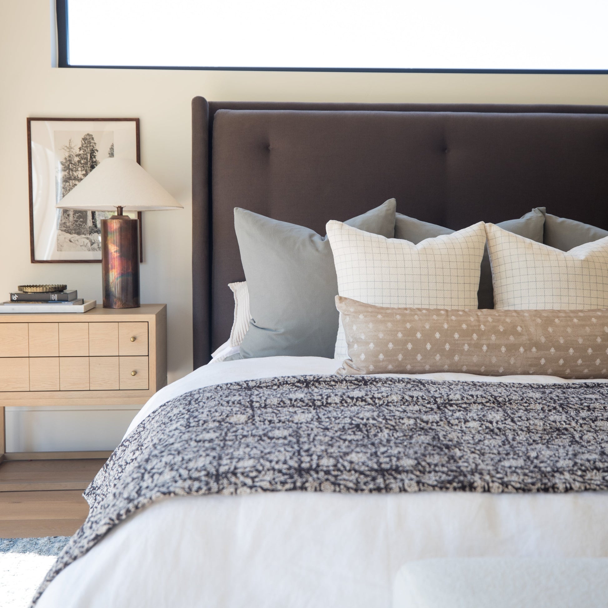 22-inch Wells Grid pillow in cream with grid pattern, displayed on bed with coordinating pillows and textured bedding.