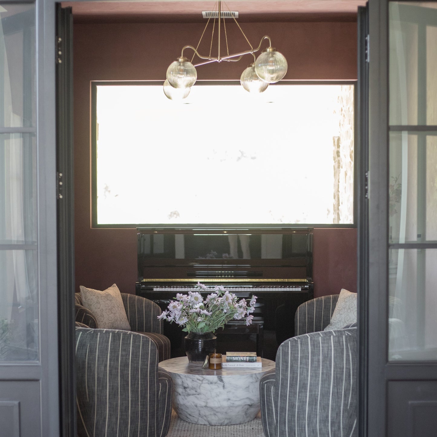 Beige striped pillow cover displayed on upholstered chair in elegant room with piano and pendant lights.