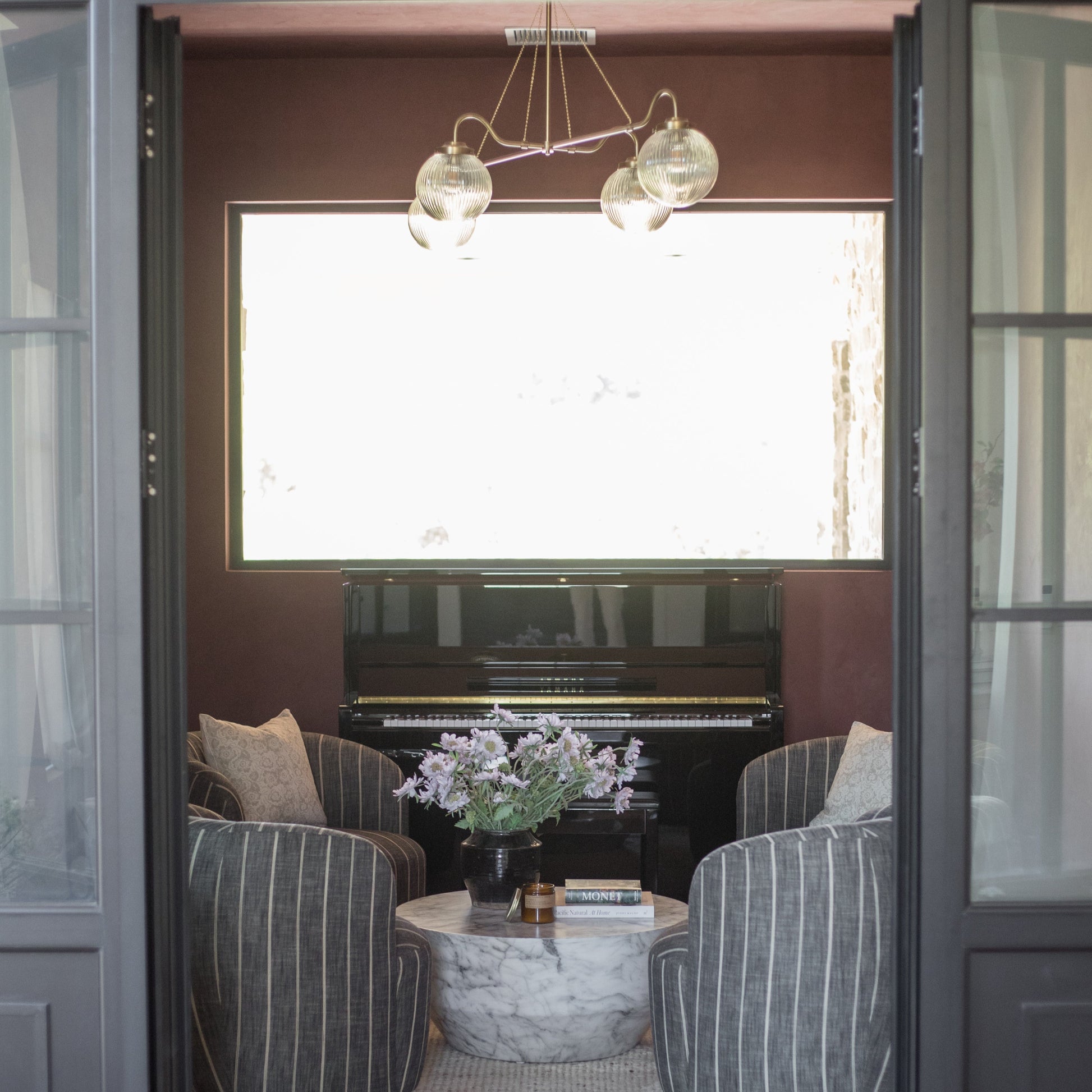 Beige striped pillow cover displayed on upholstered chair in elegant room with piano and pendant lights.