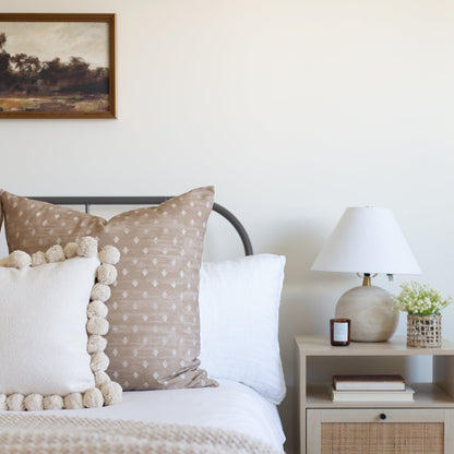 Tan linen pillow with white diamond pattern and cream pom-pom trim detail.