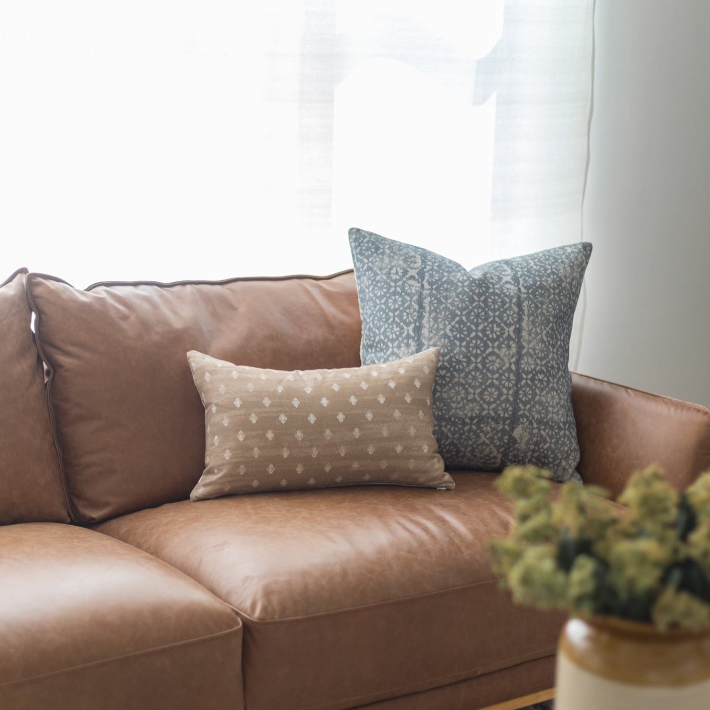 Rectangular lumbar pillow with beige geometric dot pattern displayed on brown leather sofa.