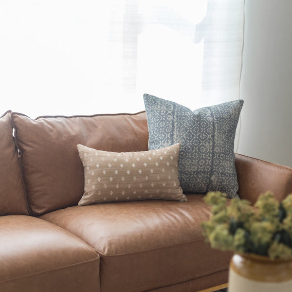 Rectangular lumbar pillow with beige geometric dot pattern displayed on brown leather sofa.