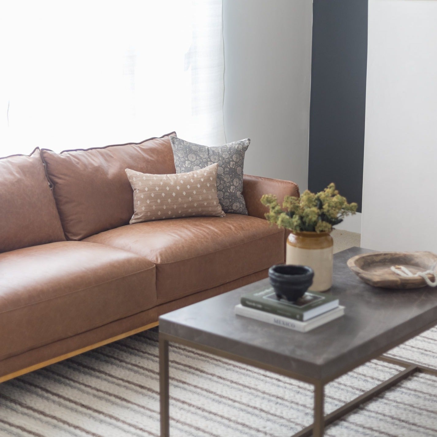 Rectangular lumbar pillow in tan with white dots and gray patterned pillow displayed on tan leather sofa.