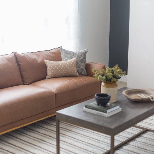 Rectangular lumbar pillow in tan with white dots and gray patterned pillow displayed on tan leather sofa.