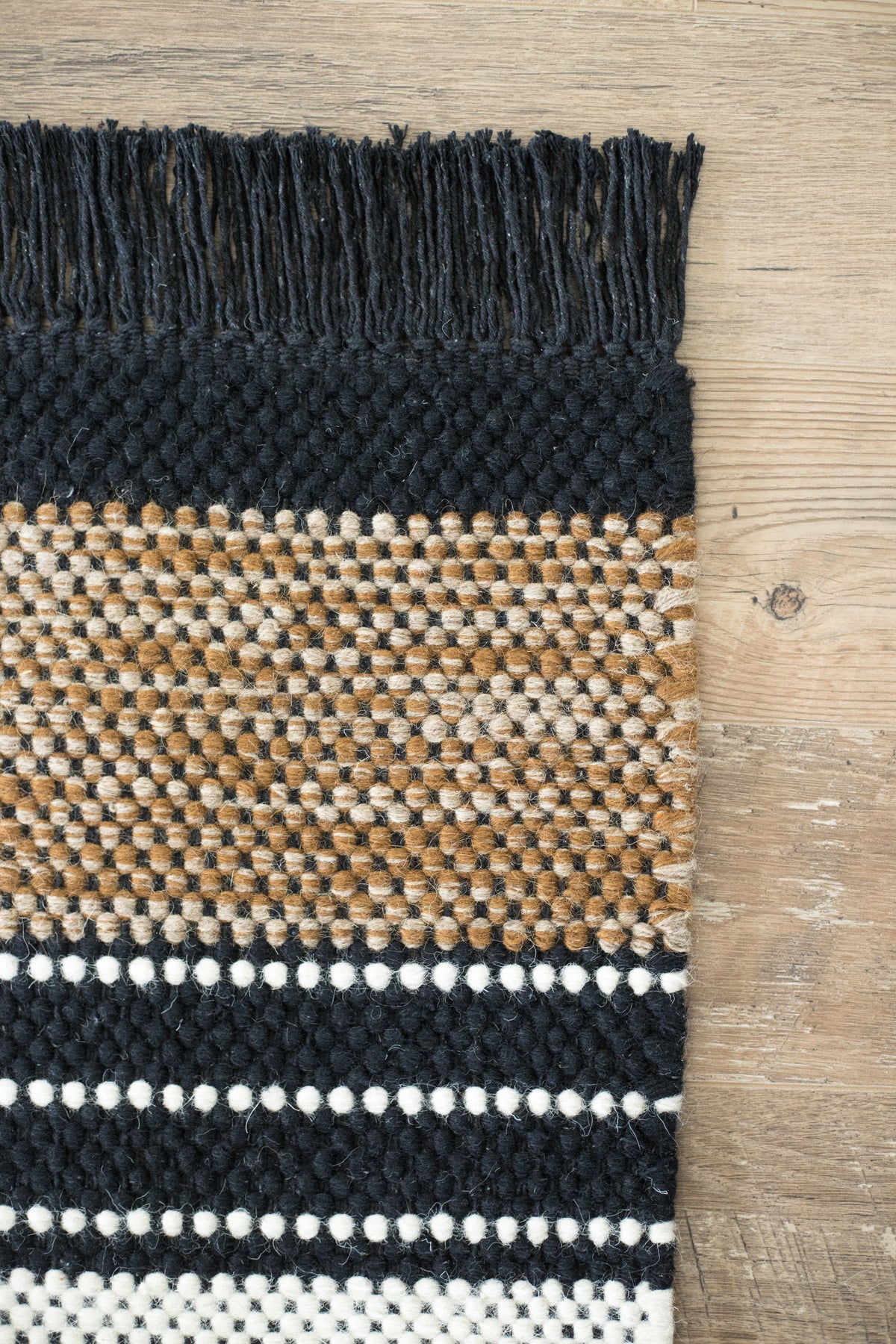 Black, tan, and cream woven runner rug with geometric striped pattern on wooden floor.