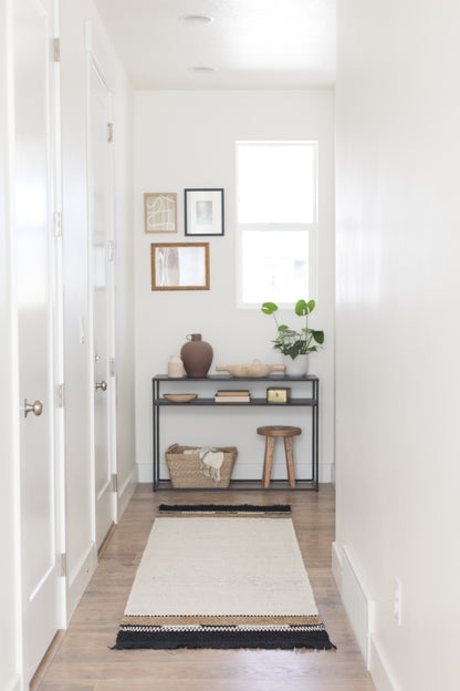 Cream and black striped runner rug with fringe trim on wood floor in entryway.