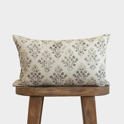 Rectangular pillow with small floral and botanical pattern in muted colors on cream background, displayed on wooden stool.