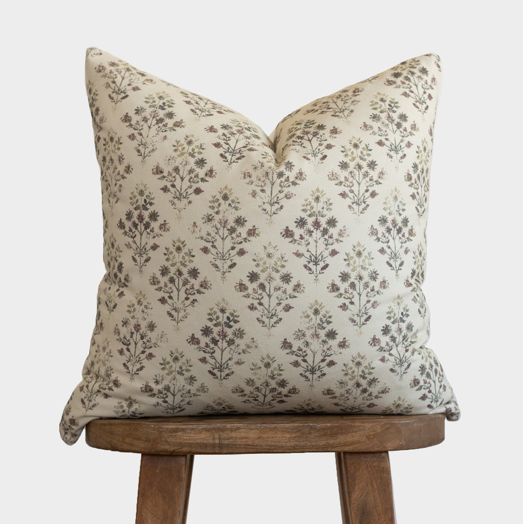 Cream pillow with brown floral botanical print, displayed on wooden tripod stool.