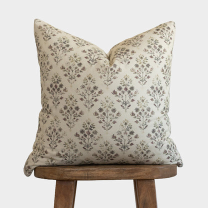 Cream pillow with brown floral botanical print, displayed on wooden tripod stool.