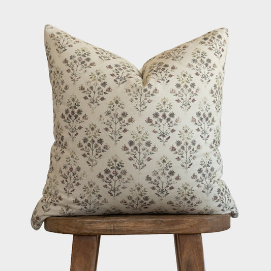 Cream pillow with brown floral botanical print, displayed on wooden tripod stool.