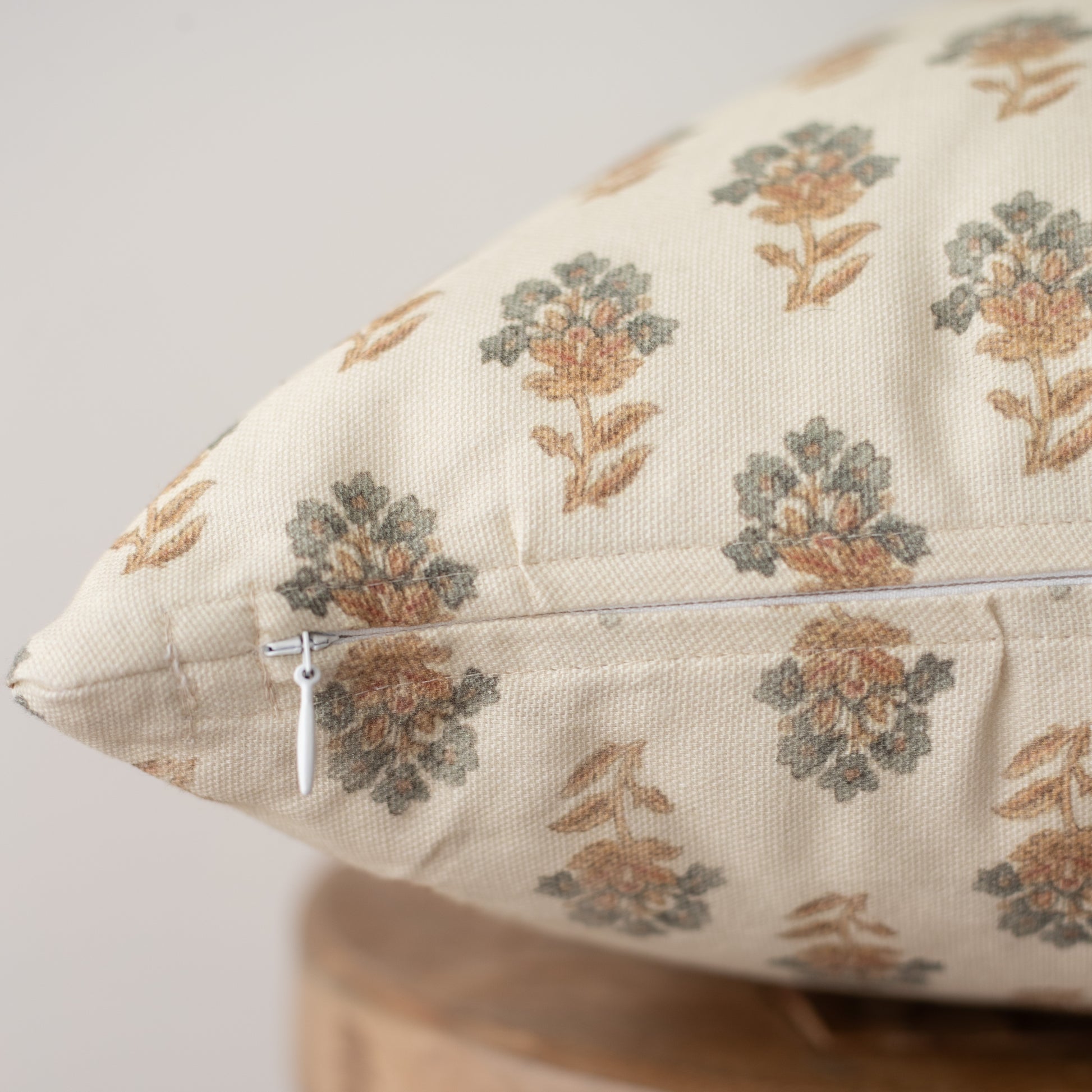 Cream throw pillow with repeating pattern of small rust and gray floral motifs, featuring a silver zipper.
