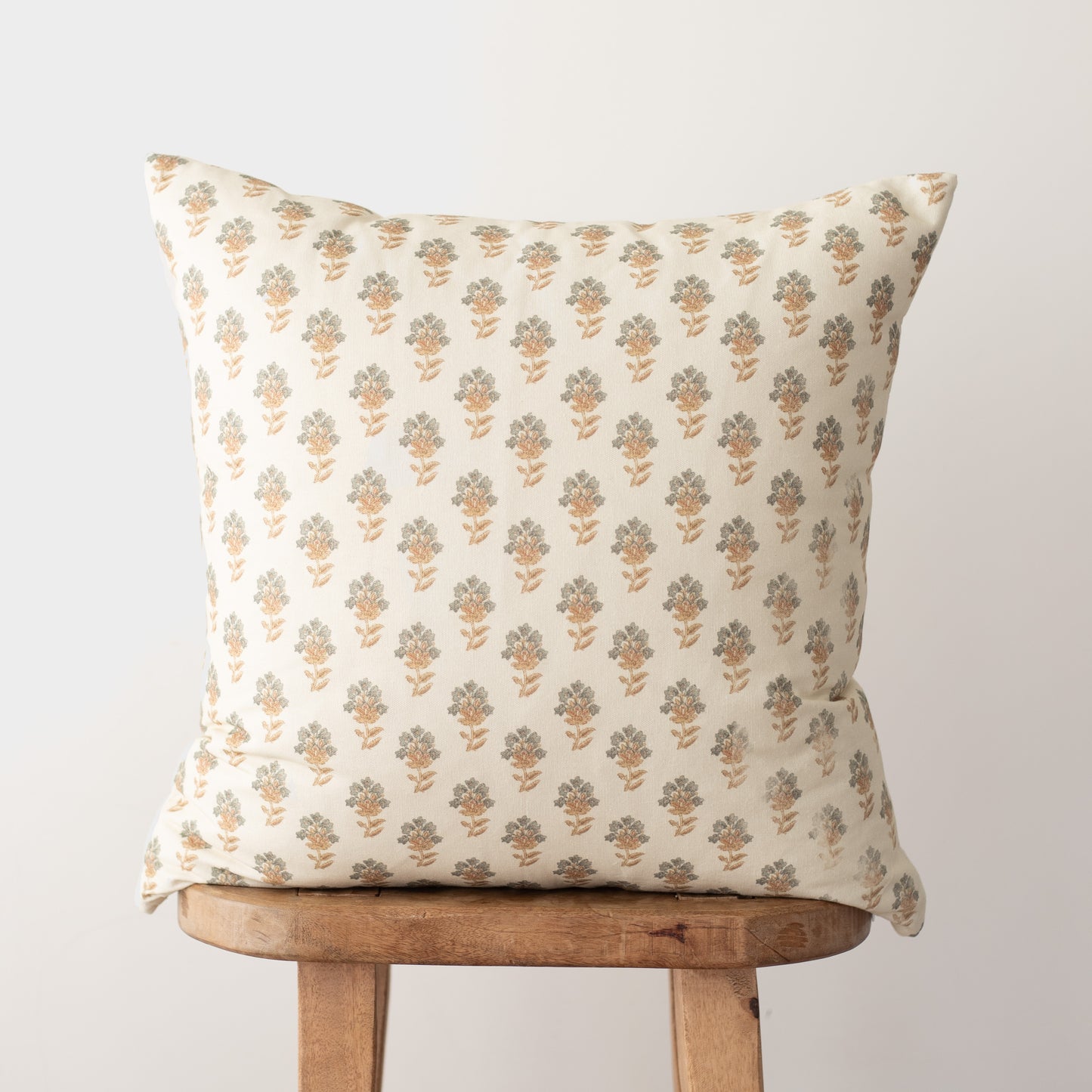 Cream pillow with small repeating gold and green floral motifs displayed on wooden stool.