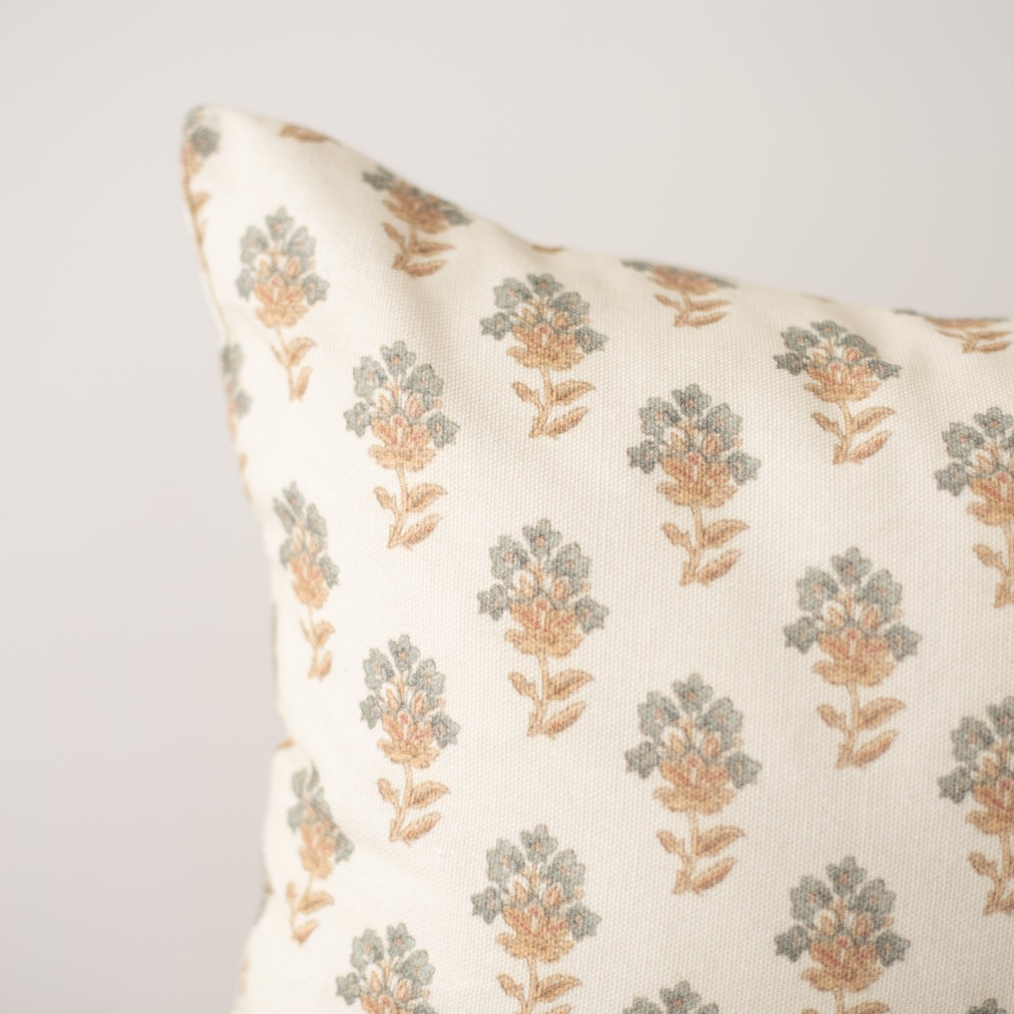 Cream pillow with repeating pattern of sage green and tan geometric flower motifs.
