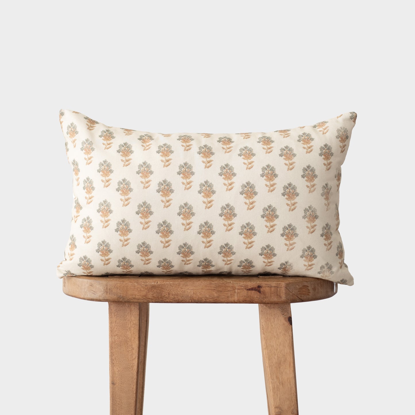 Cream pillow with repeating gold and green floral motifs displayed on a wooden stool.