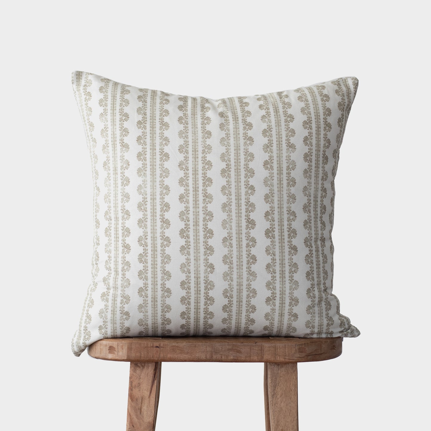 Beige and cream linen pillow with vertical striped and geometric pattern, displayed on wooden stool.