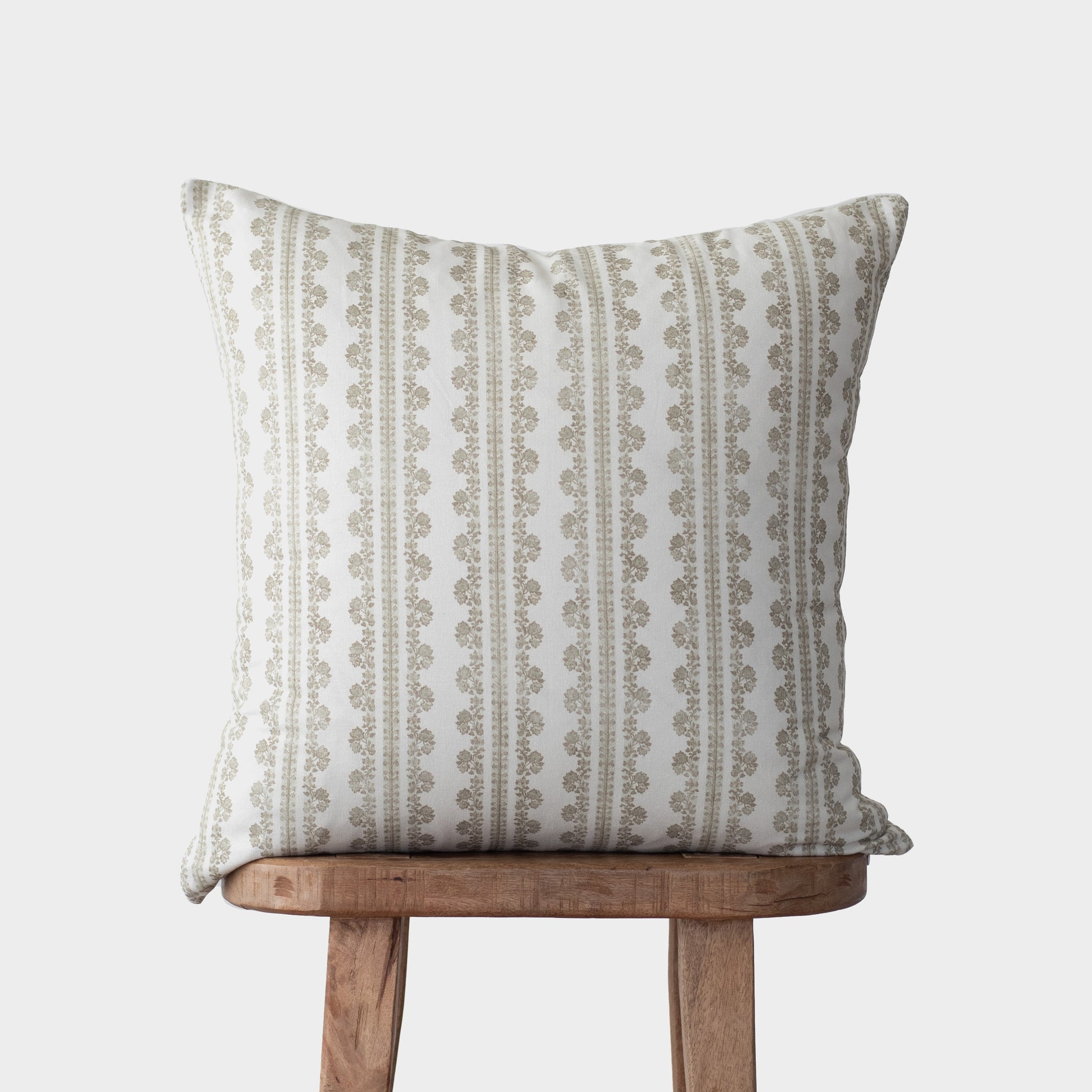 Beige and cream linen pillow with vertical striped and geometric pattern, displayed on wooden stool.