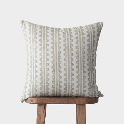 Beige and cream linen pillow with vertical striped and geometric pattern, displayed on wooden stool.