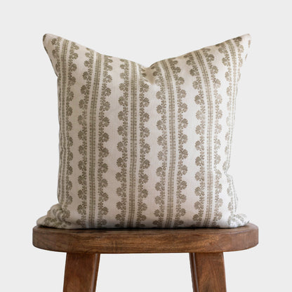 Cream linen pillow with vertical stripes and geometric floral pattern in taupe, displayed on wooden stool.