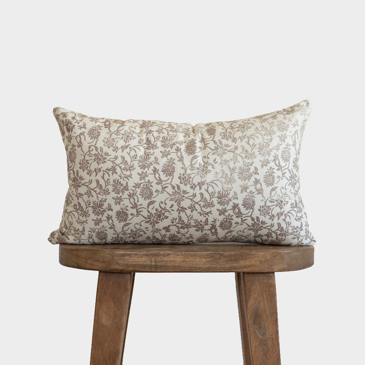 Cream linen pillow with brown floral pattern displayed on wooden stool.
