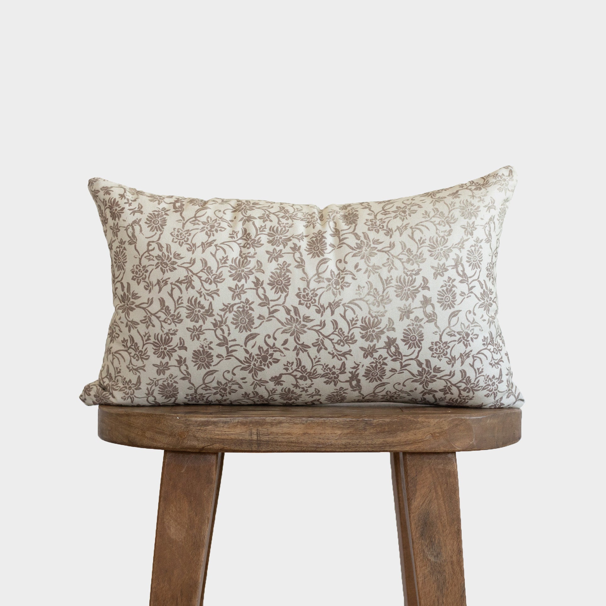 Cream linen pillow with brown floral pattern displayed on wooden stool.