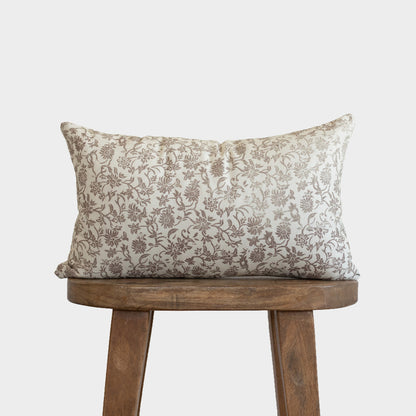 Cream linen pillow with brown floral pattern displayed on wooden stool.