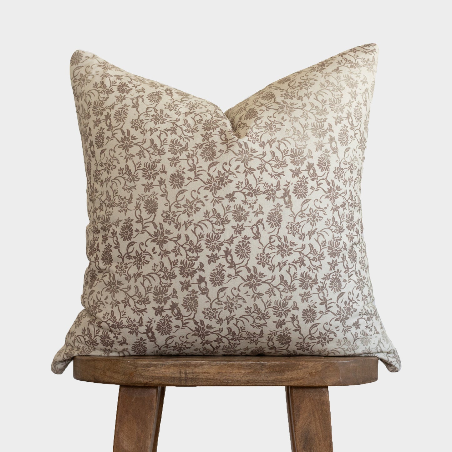 Cream and taupe floral patterned pillow cover displayed on wooden stool.