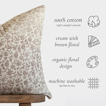 Cream cotton pillow with brown floral pattern, displayed on wooden base with care icons.