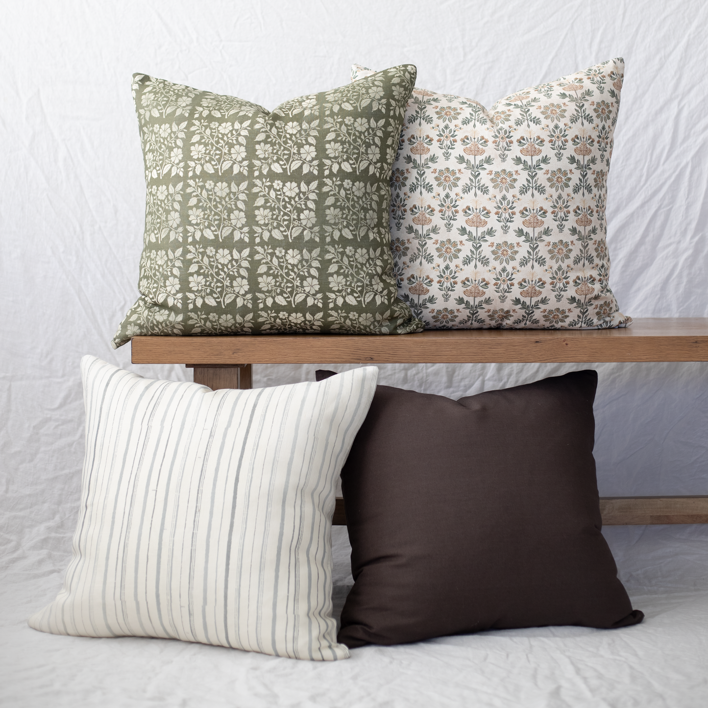 Four decorative pillows in varied patterns: sage floral, multicolor floral, cream striped, and solid brown.