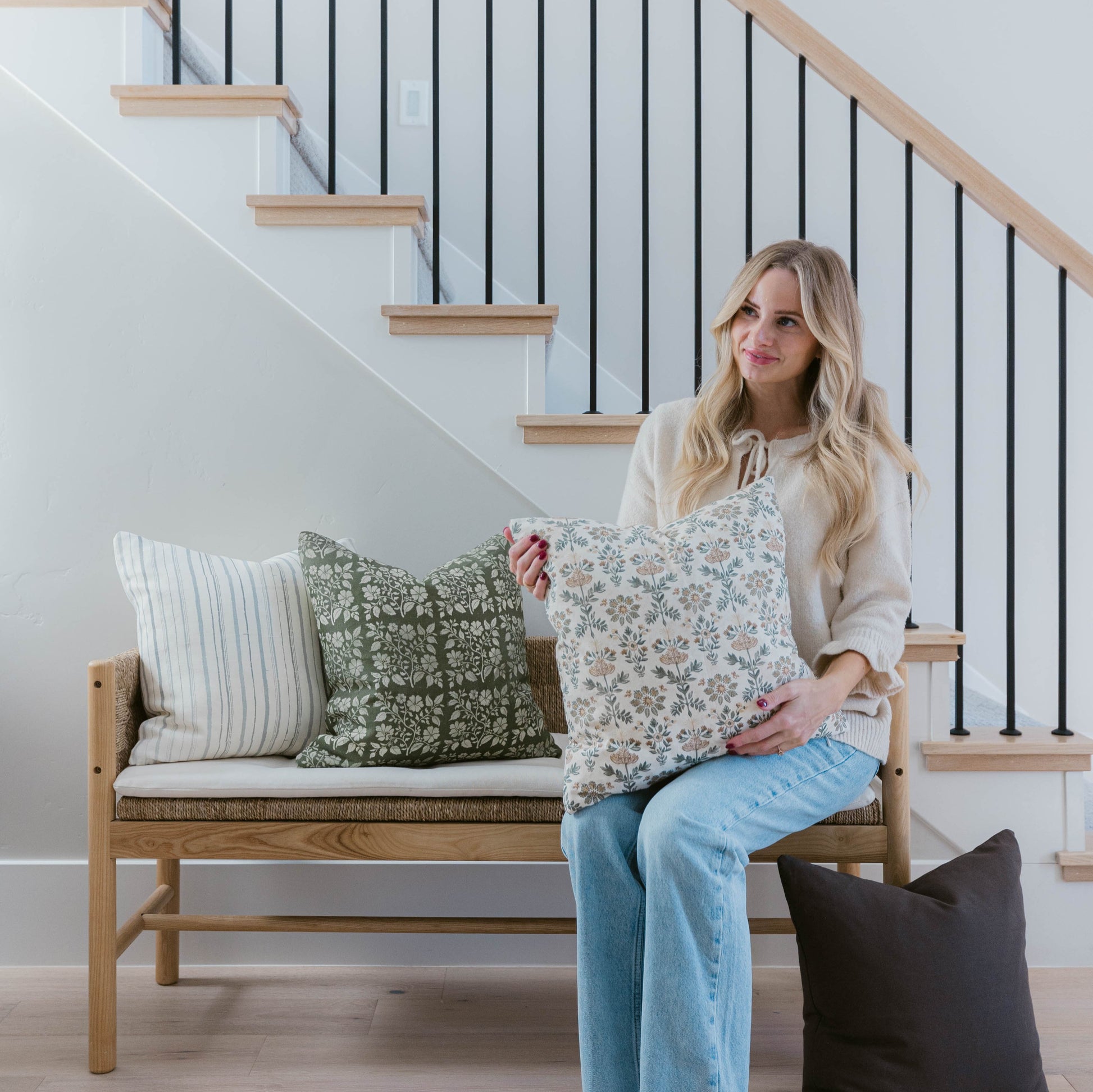 Cream linen pillow with small blue and green floral print displayed on wooden bench with striped and solid pillows.