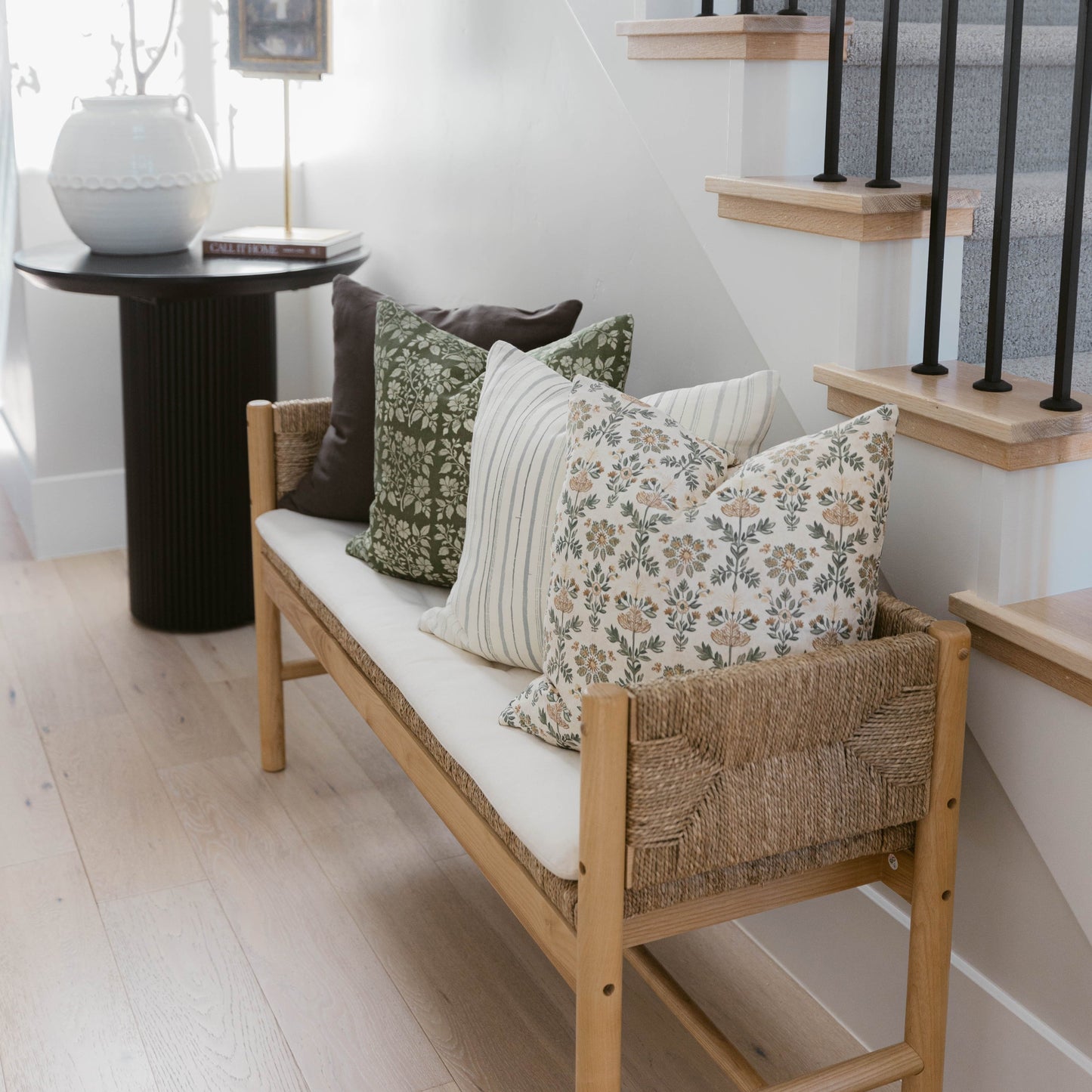 Four decorative pillows in varying patterns displayed on a wooden bench with woven sides.