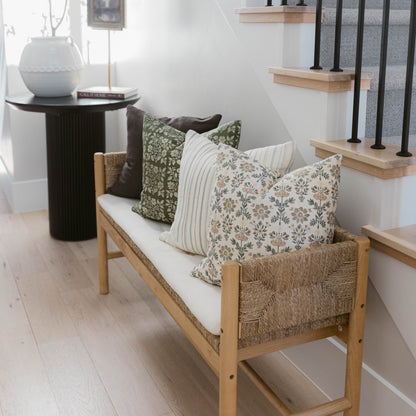 Four decorative pillows in varying patterns displayed on a wooden bench with woven sides.