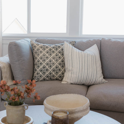Gray linen sofa with three decorative pillows featuring floral and striped patterns, positioned near a window.