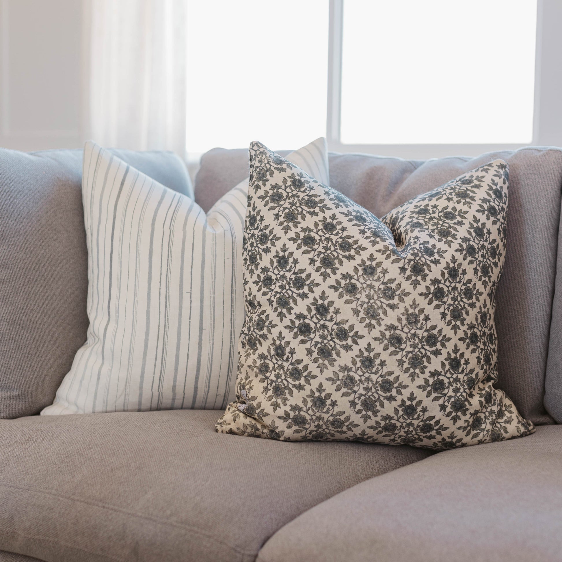 Cream linen pillow with gray vertical stripes and floral patterned pillow displayed on gray sofa.