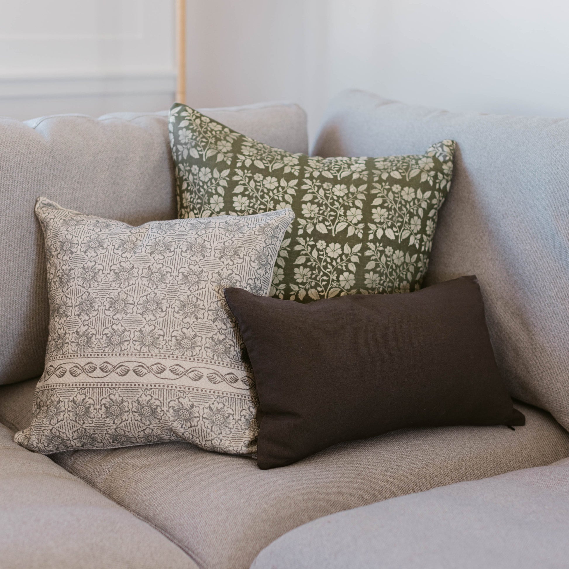 Three lumbar pillows displayed on a beige sofa: one with cream and taupe geometric pattern, one with olive green floral print