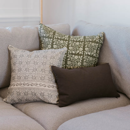 Three lumbar pillows displayed on a beige sofa: one with cream and taupe geometric pattern, one with olive green floral print