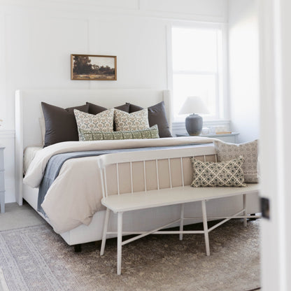 Green and cream floral patterned linen pillow displayed on a bed with black and neutral bedding.