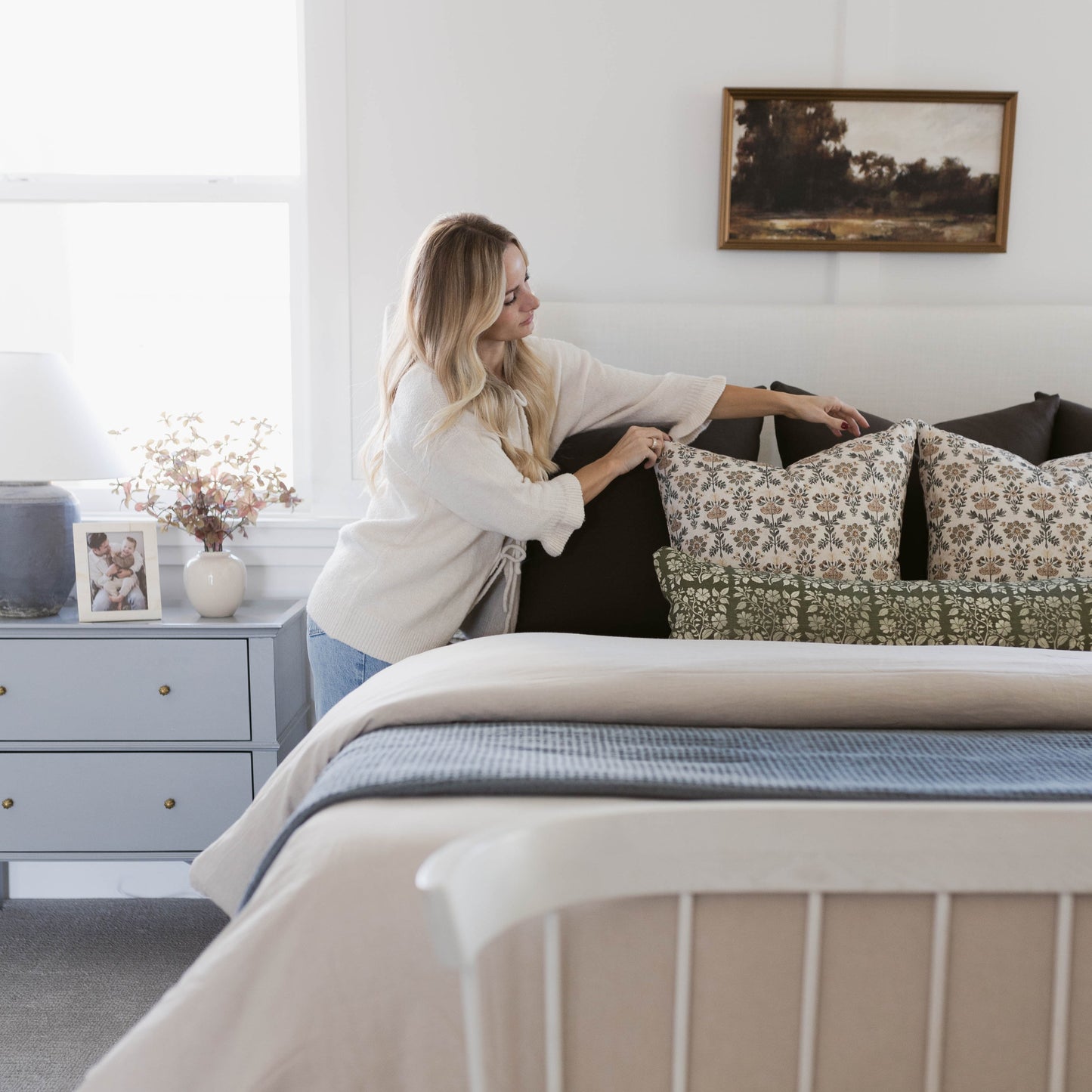 Rectangular lumbar pillow with green and cream floral pattern displayed on a bed with black headboard and bedding.