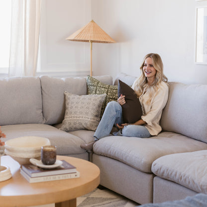 Rectangular lumbar pillow with double-sided design in neutral tan and olive green patterns displayed on beige sectional sofa.