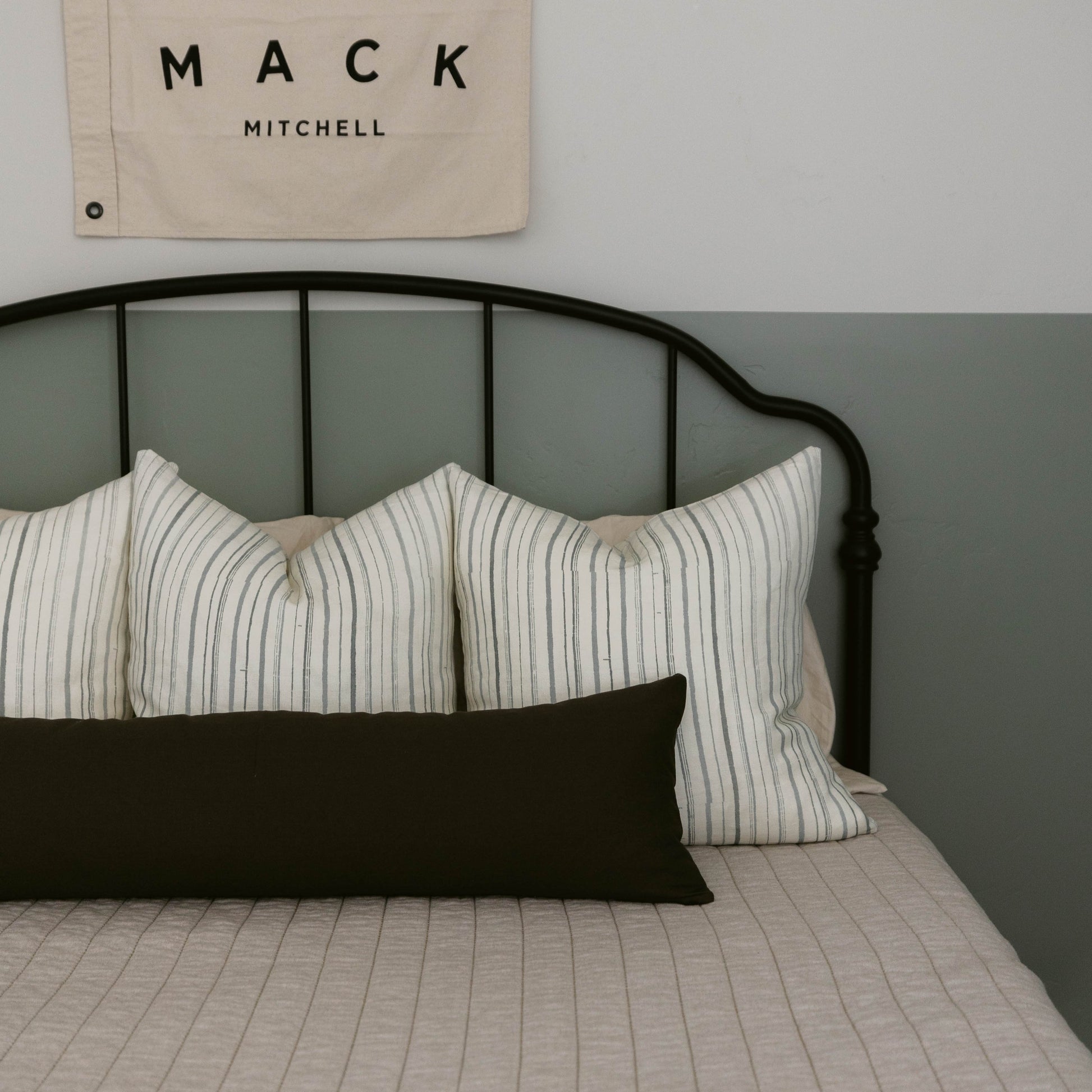Black lumbar pillow with white striped pillows on metal bed frame.