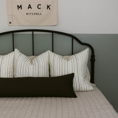 Black lumbar pillow with white striped pillows on metal bed frame.
