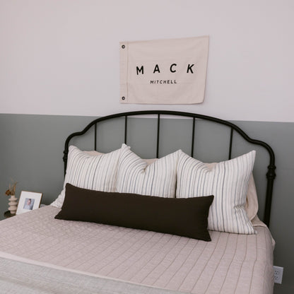 Black double-sided lumbar pillow on bed with striped pillows and quilted bedding.