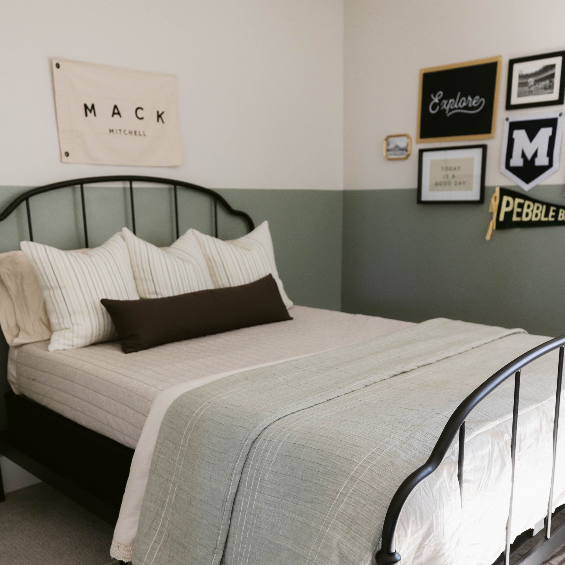 Black rectangular lumbar pillow displayed on a bed with striped pillows and a gray quilted throw.